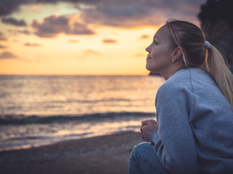 woman sits out on the beach practicing the art of mindfulness in recovery