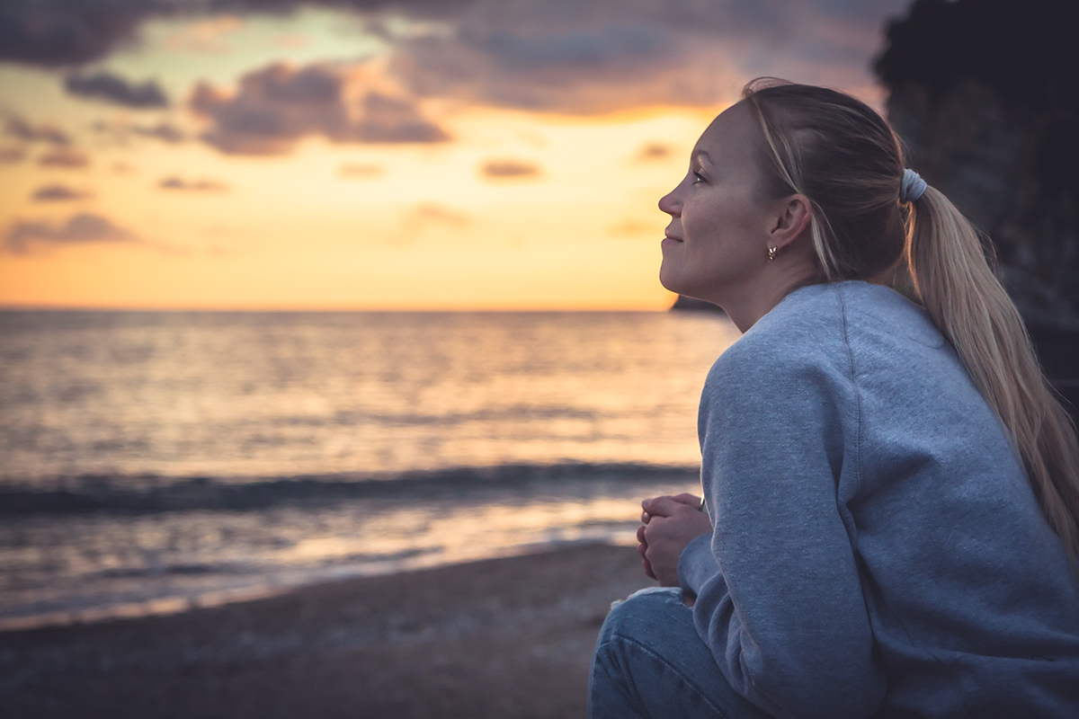 woman sits out on the beach practicing the art of mindfulness in recovery