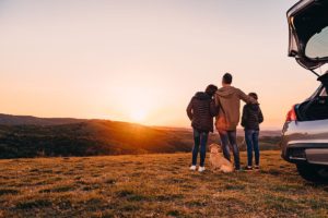 our mission, family of three watching the sunset next to their car on a hillside