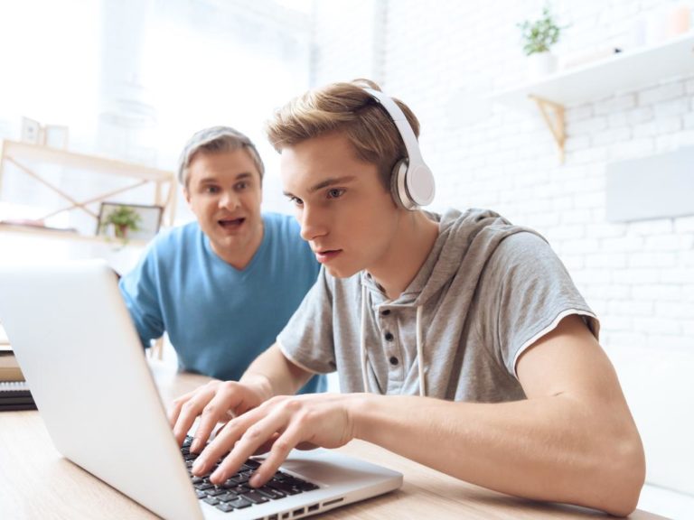Teen wearing headphones playing on computer and ignoring father