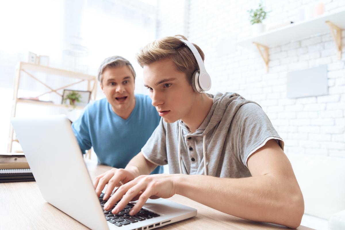 Teen wearing headphones playing on computer and ignoring father