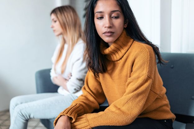 person in yellow sweater looks away from other person on couch while discussing compulsive reassurance seeking