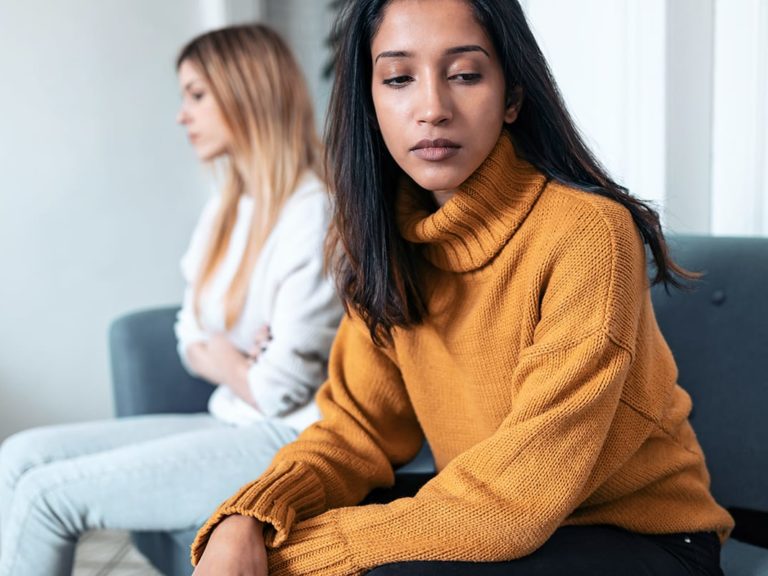 person in yellow sweater looks away from other person on couch while discussing compulsive reassurance seeking