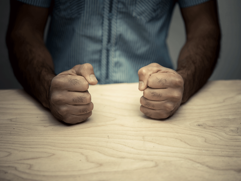 person puts fists on table while learning about anger cues