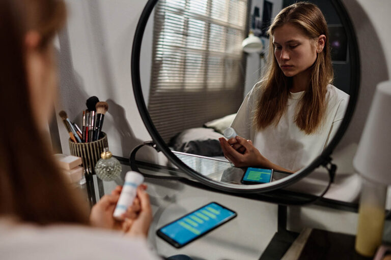 teenage girl looks at prescription drug bottle in mirror