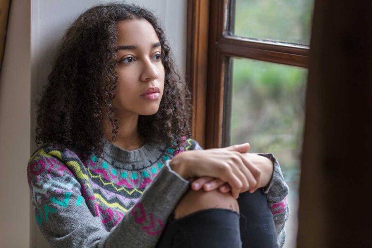 teen sitting next to window considers the impact of chronic illness on mental health