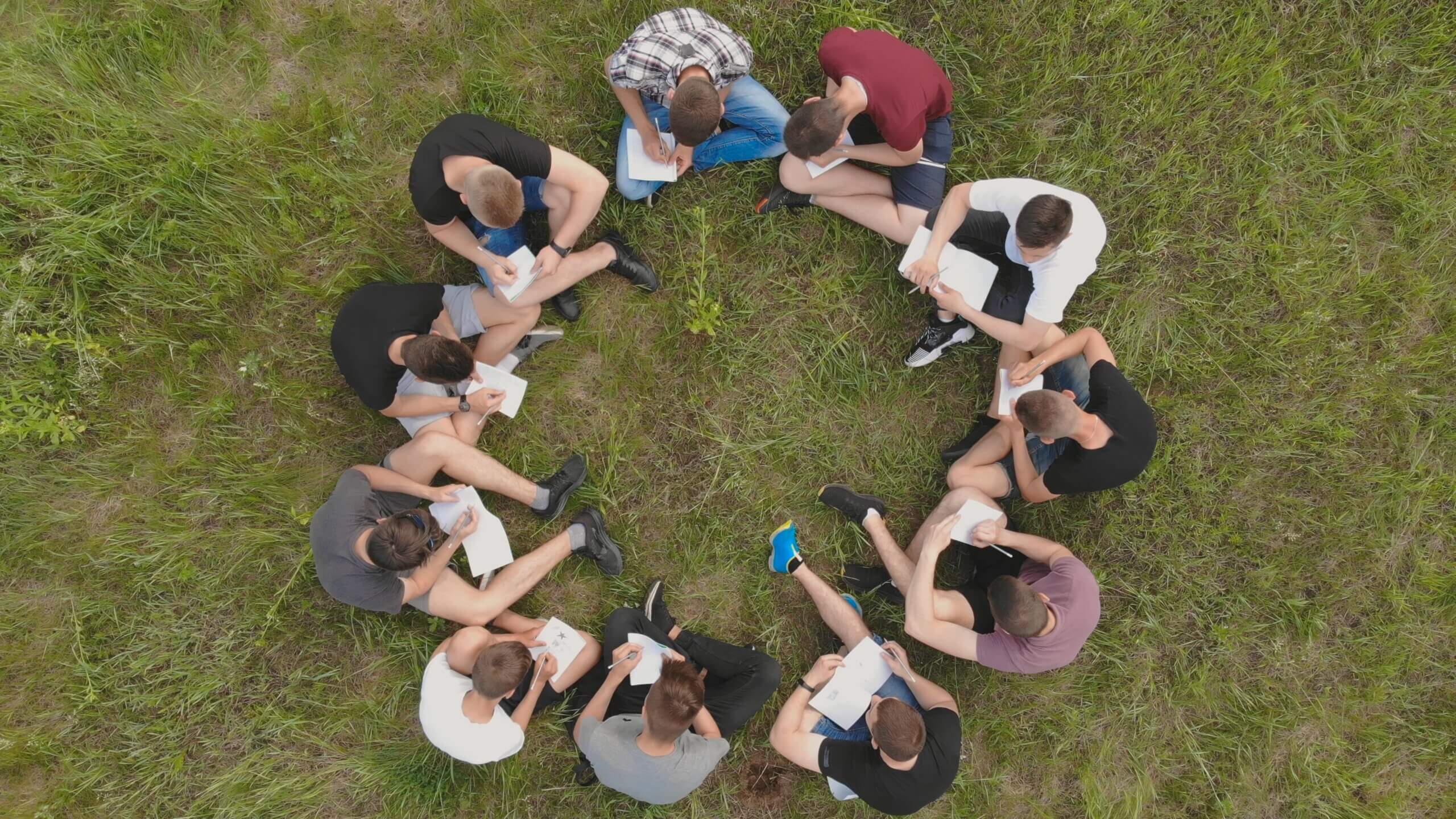 Teamwork concept. A group of high school students sit on the grass in a circle. Drone view.